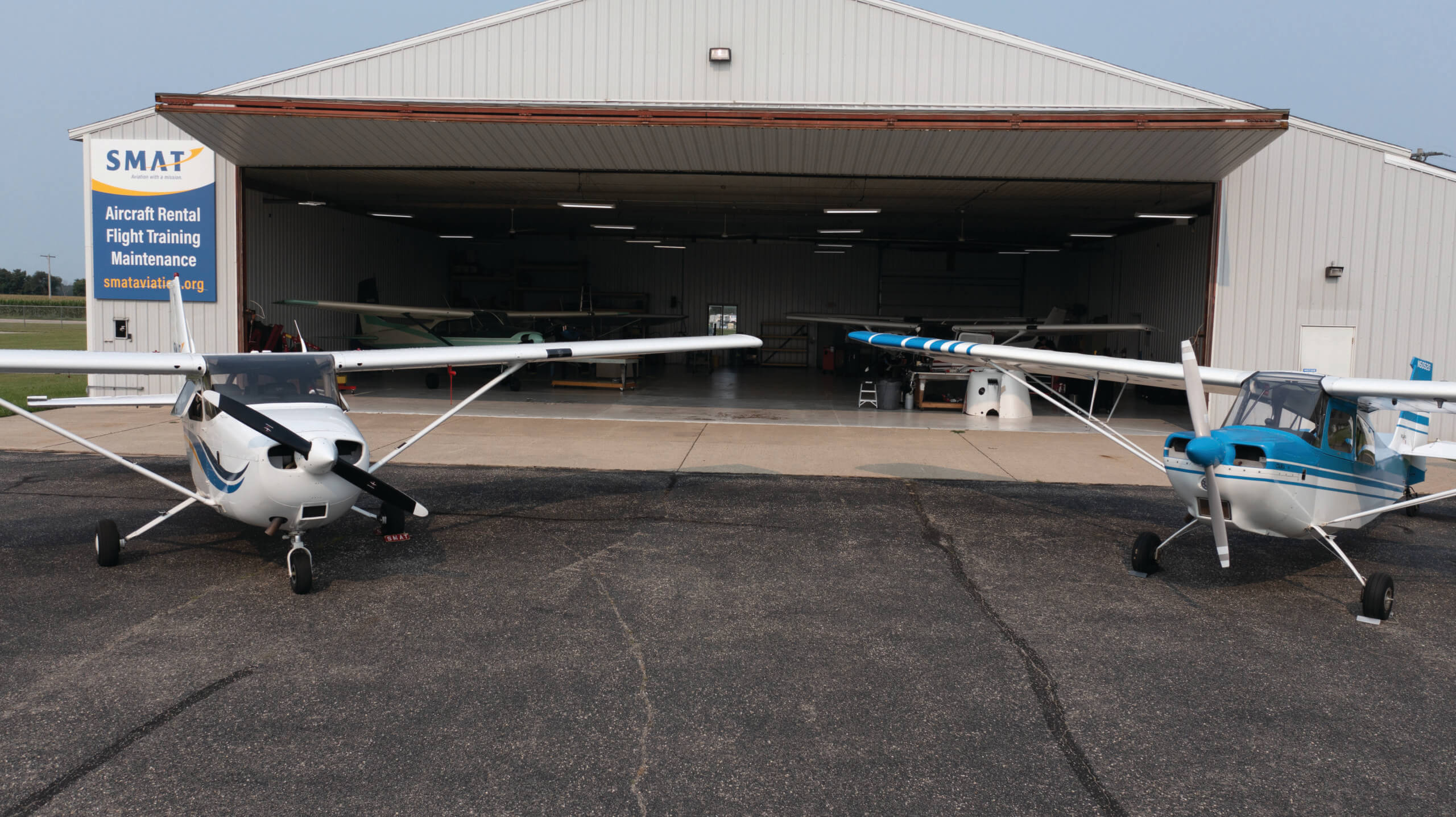 Image of two small airplanes parked outside of a large SMAT garage. 