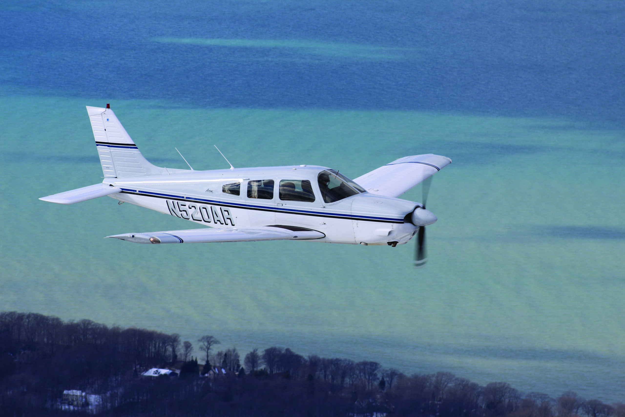 Image of a small, white airplane flying over a bright blue ocean.